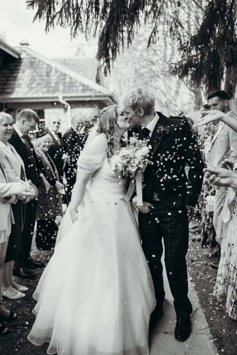 Bride and groom sharing a kiss in a confetti shower outside their Scottish wedding venue