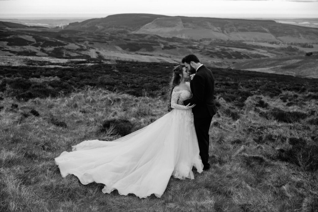 Bride and groom embrace in black-and-white portrait on Cairn o' Mount hillside near Drumtochty Castle, Aberdeenshire, with sweeping Highland moorland backdrop